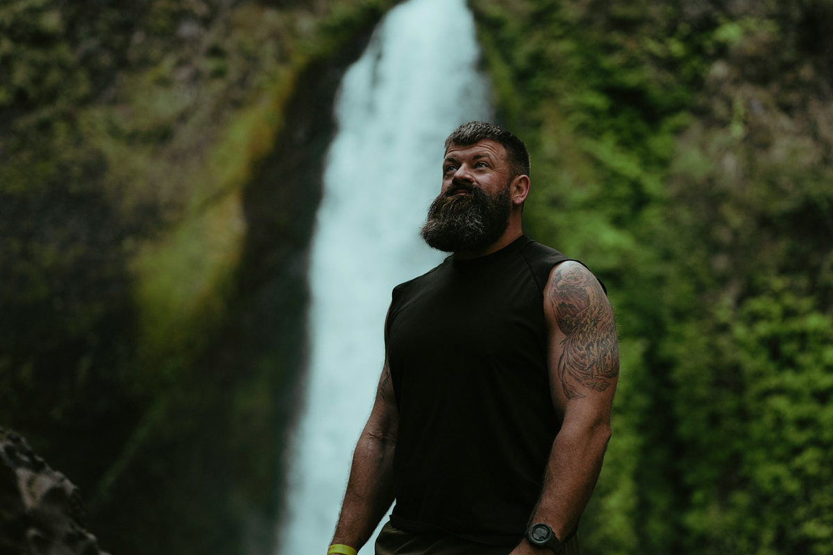 Imagem de um modelo masculino posando ao lado de uma cachoeira